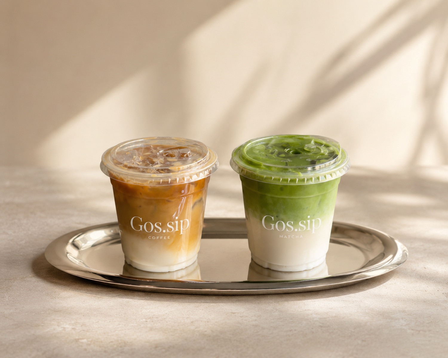 Gos.sip iced matcha and iced coffee side by side on a silver tray